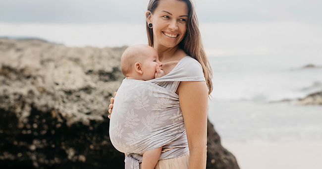 Madre porteando a su bebé en la playa con fular portabebés elástico de Love and Carry