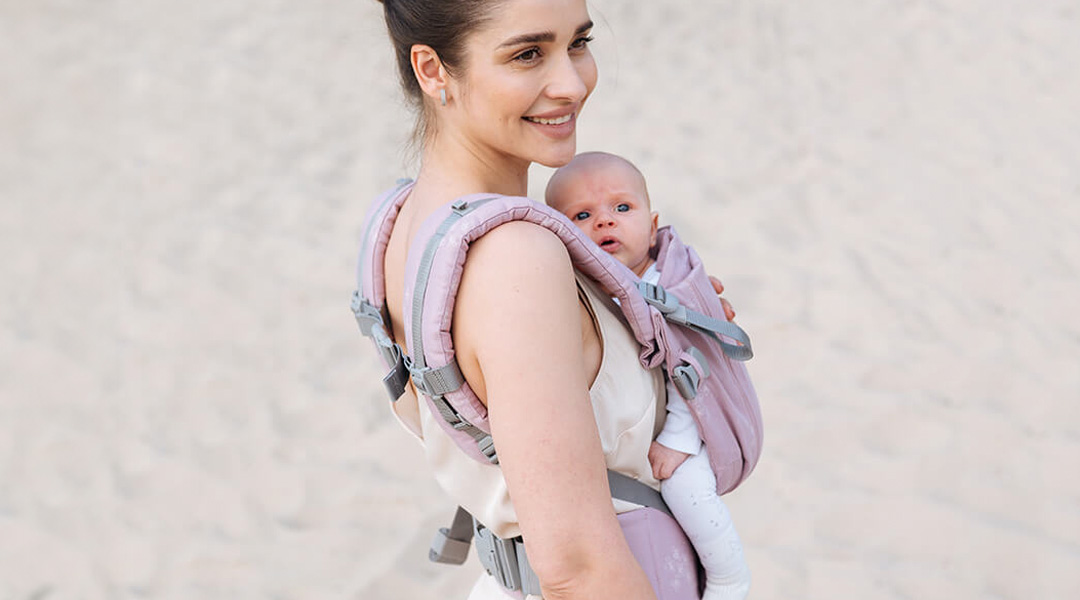 Madre paseando en playa con su bebé en la mochila portabebés ONE