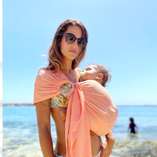 Madre y bebé usando la bandolera Quokkababy en la playa